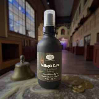 Bottle of 'Bellhop's Curse' room & linen spray with a blurred eerie hallway background