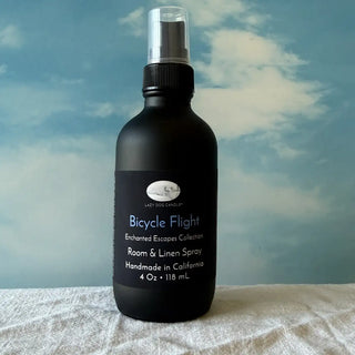 Black room & linen spray bottle labeled 'Bicycle Flight' against a blue sky background