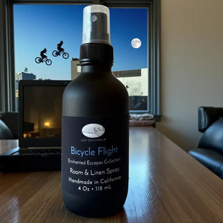 Room & Linen Spray bottle labeled 'Bicycle Flight' on a desk with a window view.