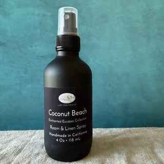 Black room & linen spray bottle labeled 'Coconut Beach' on a textured surface with teal background
