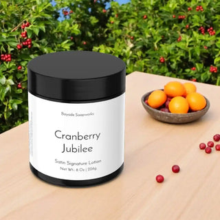 Lotion jar labeled 'Cranberry Jubilee' by Bayside Soapworks on a wooden surface with cranberries and oranges.