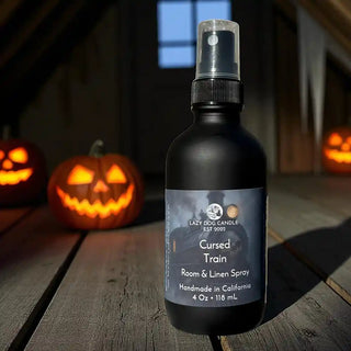 Bottle of 'Cursed Train' room & linen spray with pump on a wooden surface with Halloween pumpkins in the background.