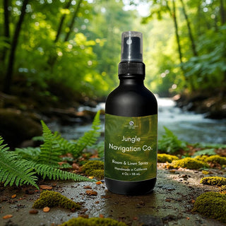 Jungle Navigation Co. room & linen spray bottle in a natural setting with greenery and water.