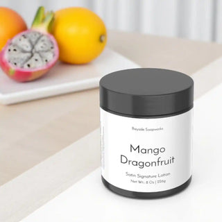 Lotion jar labeled 'Mango Dragonfruit' by Beyode Soapworks on a light surface with dragonfruit in the background.