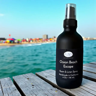 Black spray bottle labeled 'Ocean Beach Escape' on a wooden dock with a beach background