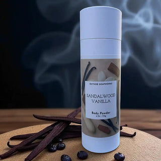Body powder bottle labeled 'Sandalwood Vanilla' with vanilla beans and vanilla flowers on a dark background.