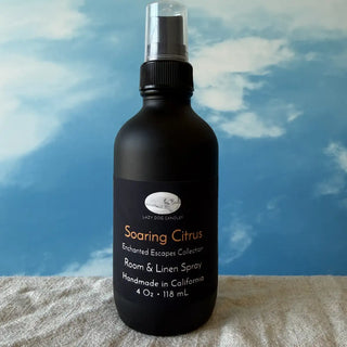 Black room and linen spray bottle labeled 'Soaring Citrus' against a blue sky background