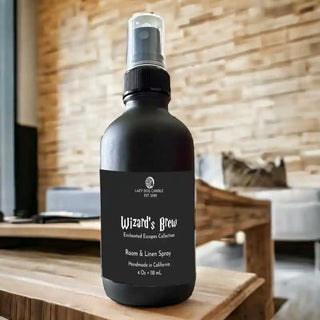 Black room spray bottle labeled 'Wizard's Brew' on a wooden surface with a blurred indoor background.